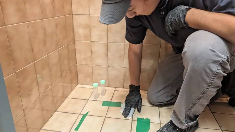 Dust wipe sample being collected from a ceramic tile floor beside sample vials