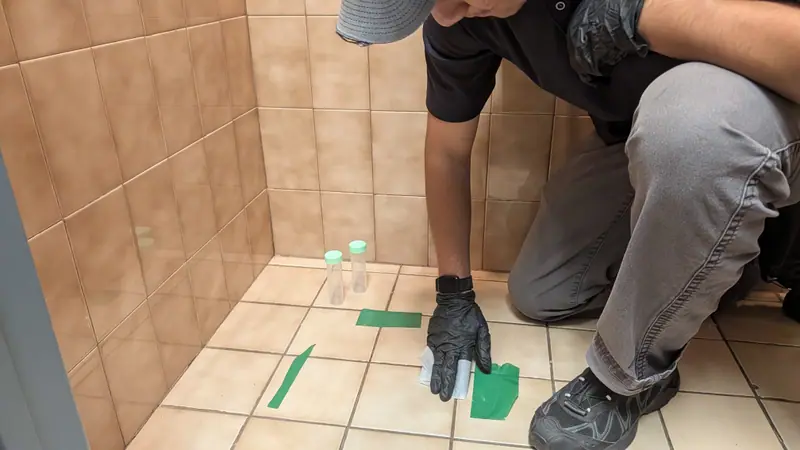 Sample vials and a green-tape template on a tile floor during dust wipe clearance testing