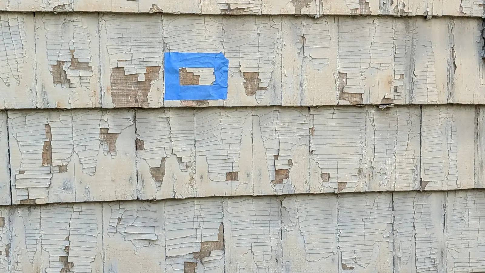 Blue tape marking a paint chip sample location on peeling exterior paint