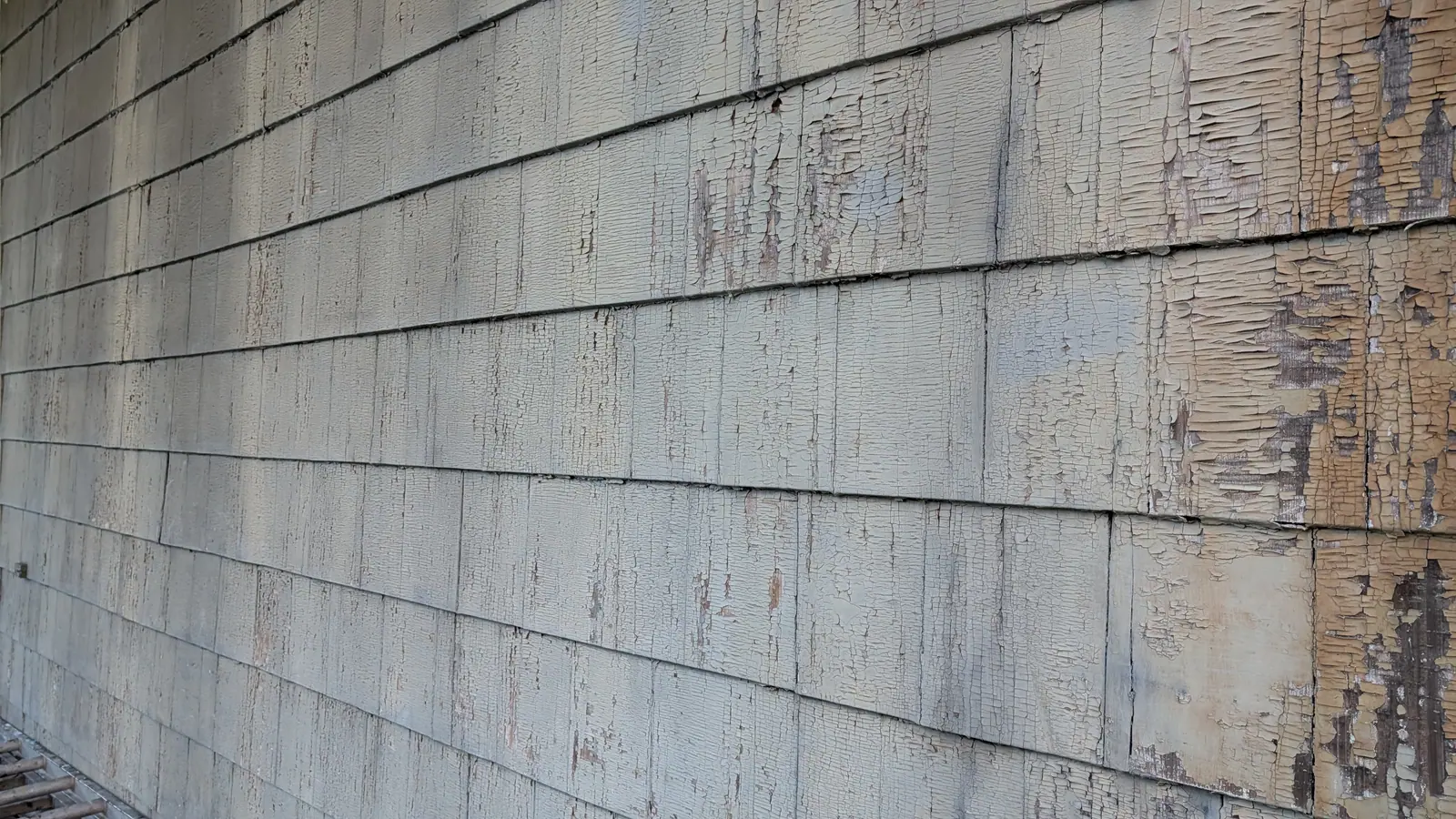 Cracked and peeling paint on the exterior wood siding of an older New York City building, a common lead paint hazard