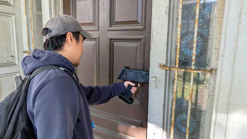Inspector using a SciAps X550PB XRF analyzer on a painted door for a Local Law 31 inspection