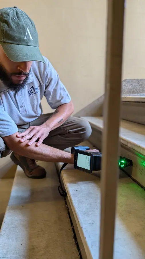 Inspector crouching in a stairwell scanning the steps with a handheld XRF analyzer