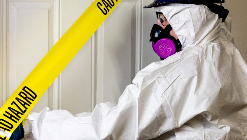 Worker in a protective suit and respirator beside yellow caution tape