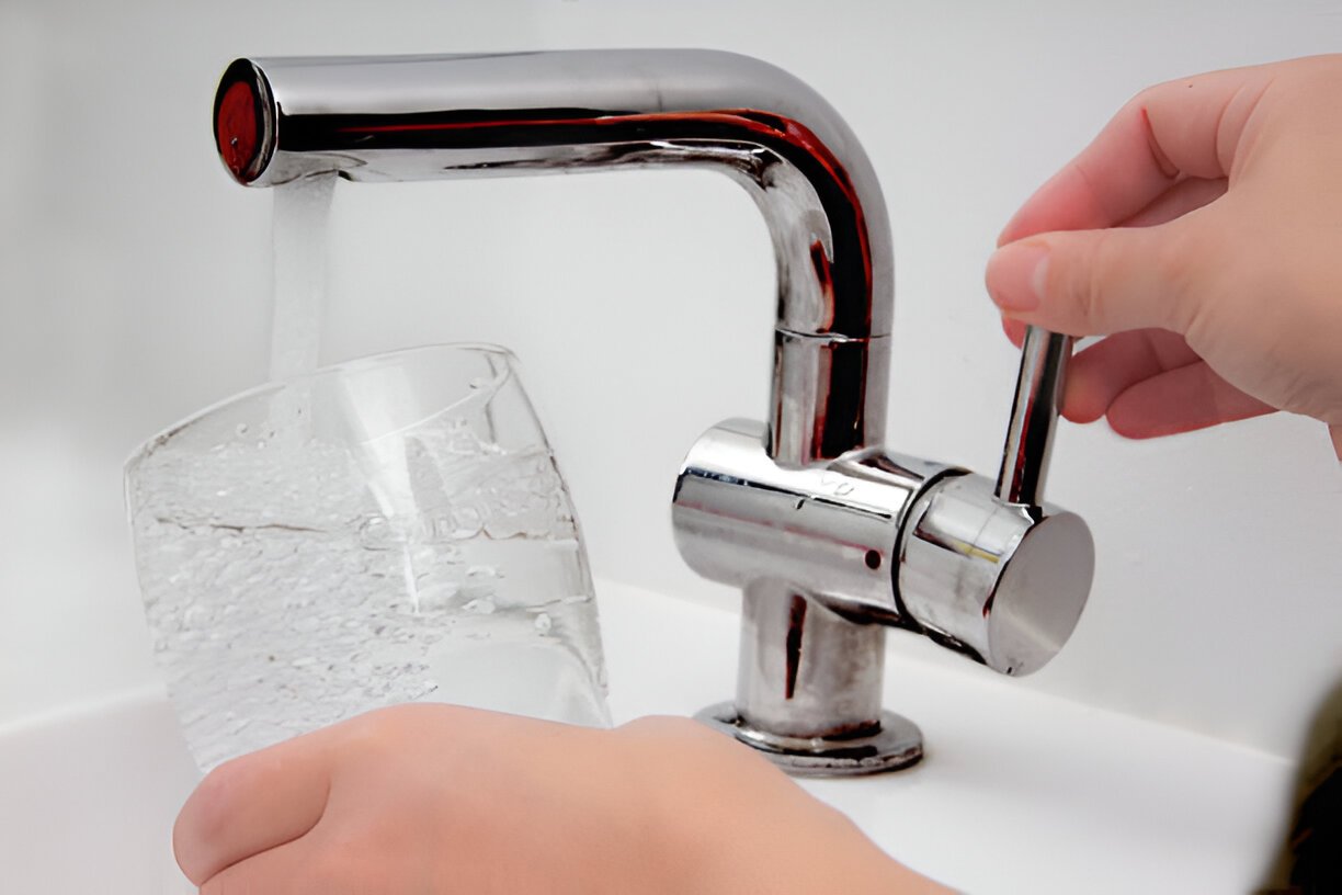 Hand turning a faucet to fill a glass with water